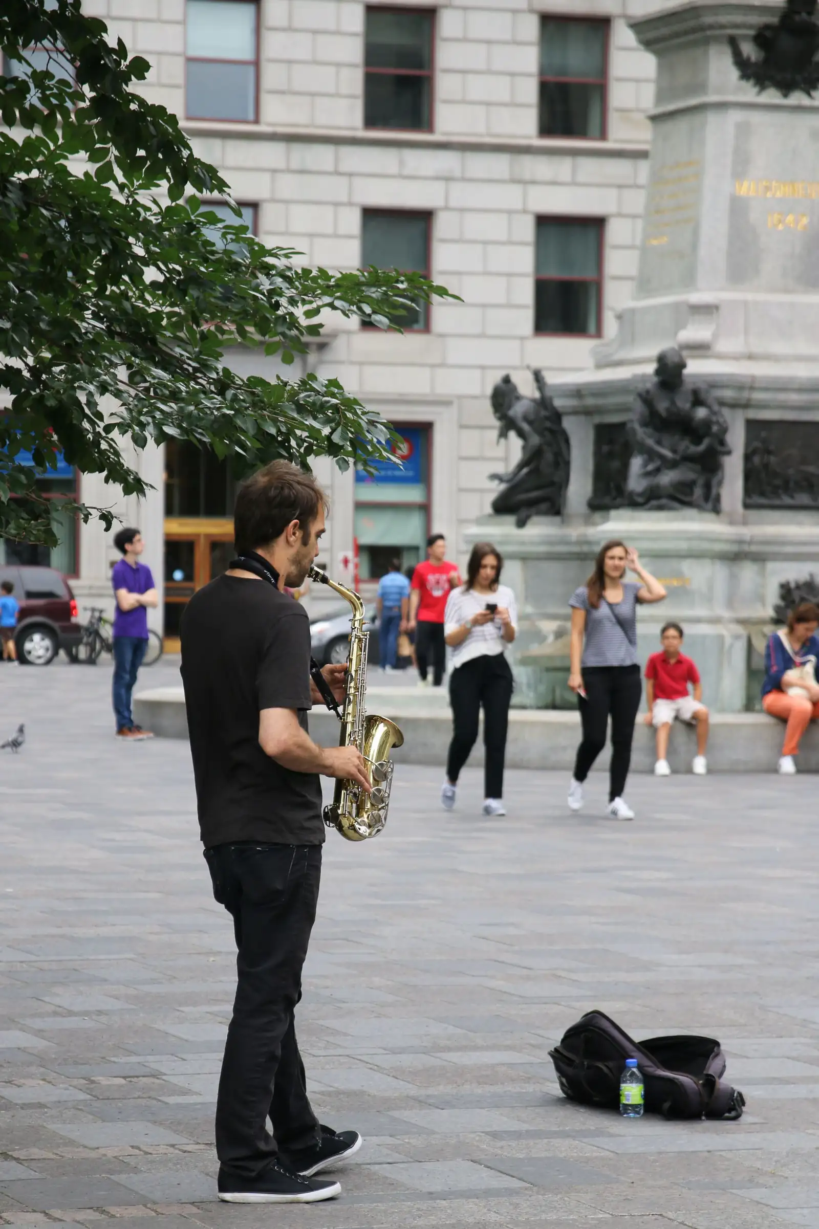 A street musician playing saxophone in a Montreal public square as people walk past